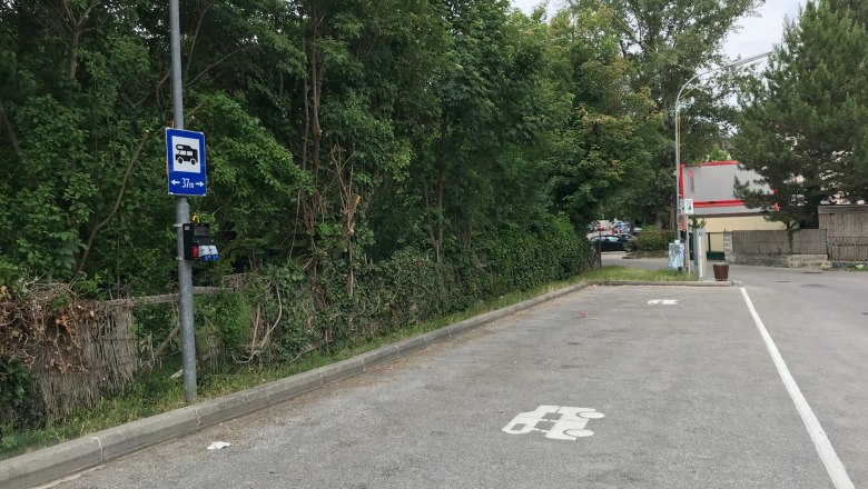 Parkplatz für Wohnmobile mit Stromanschluss, umgeben von Bäumen.