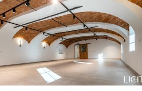 Leerer Veranstaltungsraum mit gewölbter Ziegeldecke und Holztür.