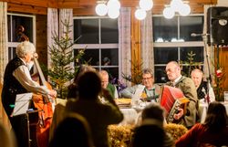 Musikanten sitzen rund um einen Holztisch in einer Hütte in weihnachtlichem Ambiente