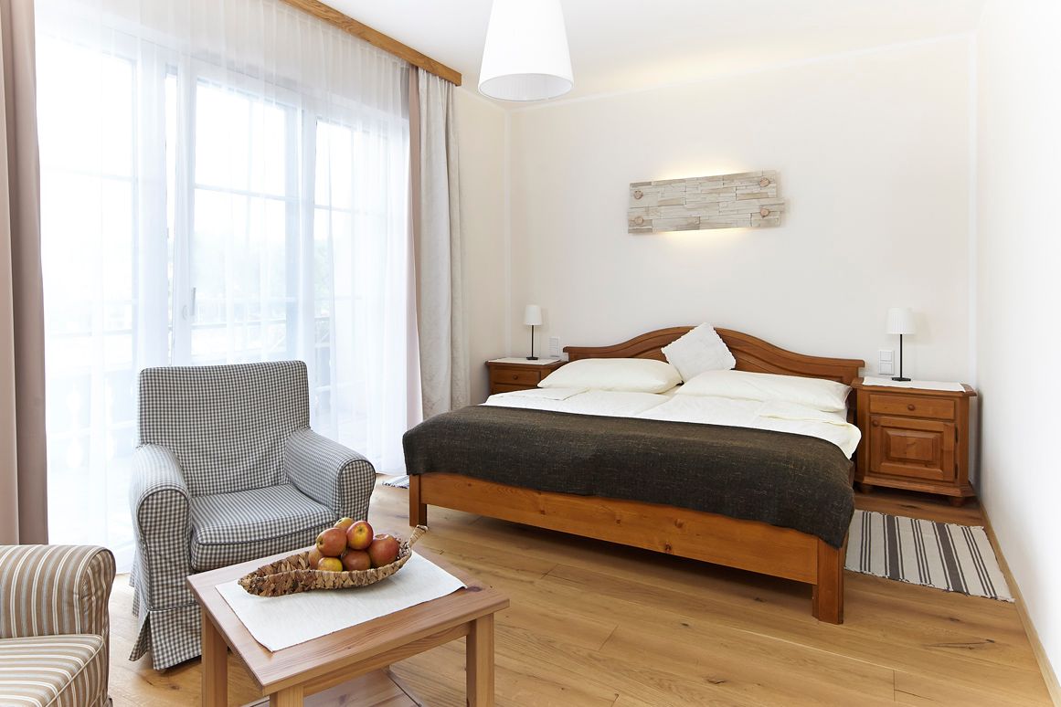 Helles Zimmer mit Doppelbett, Sessel und Tisch mit Obstschale.