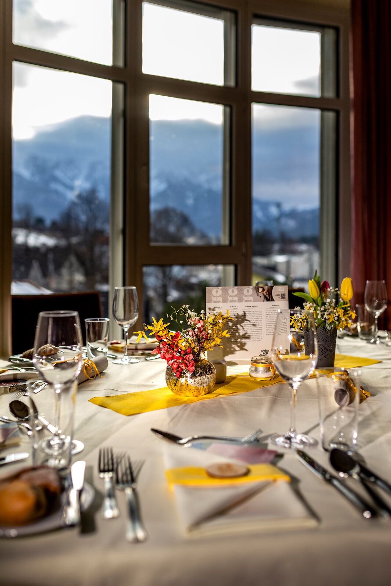 Fein gedeckter Tisch vor einem Fenster mit Bergblick bei der Kulinarik-Veranstaltung Gedanken-Gänge im Hotel Schneeberghof.
