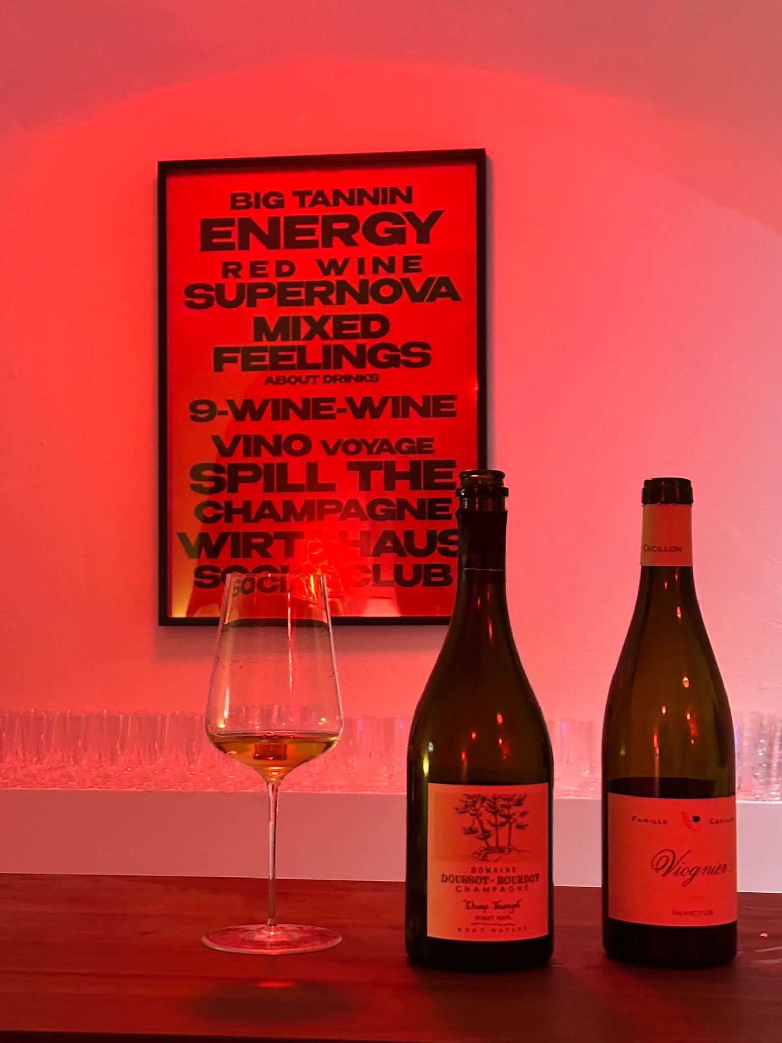 Weinflaschen und Weißweinglas im roten Ambiente der Bar