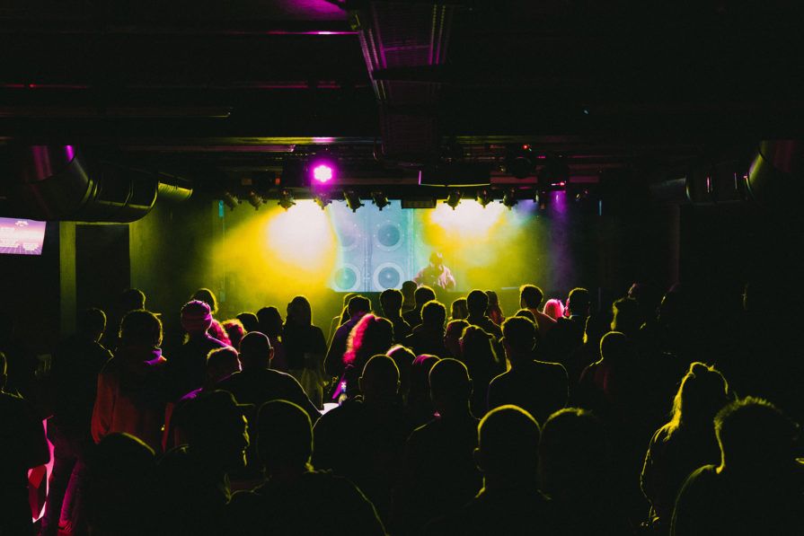 Livekonzert auf einer beleuchteten Bühne mit Band. Jubelndes Publikum ist im Vordergrund.