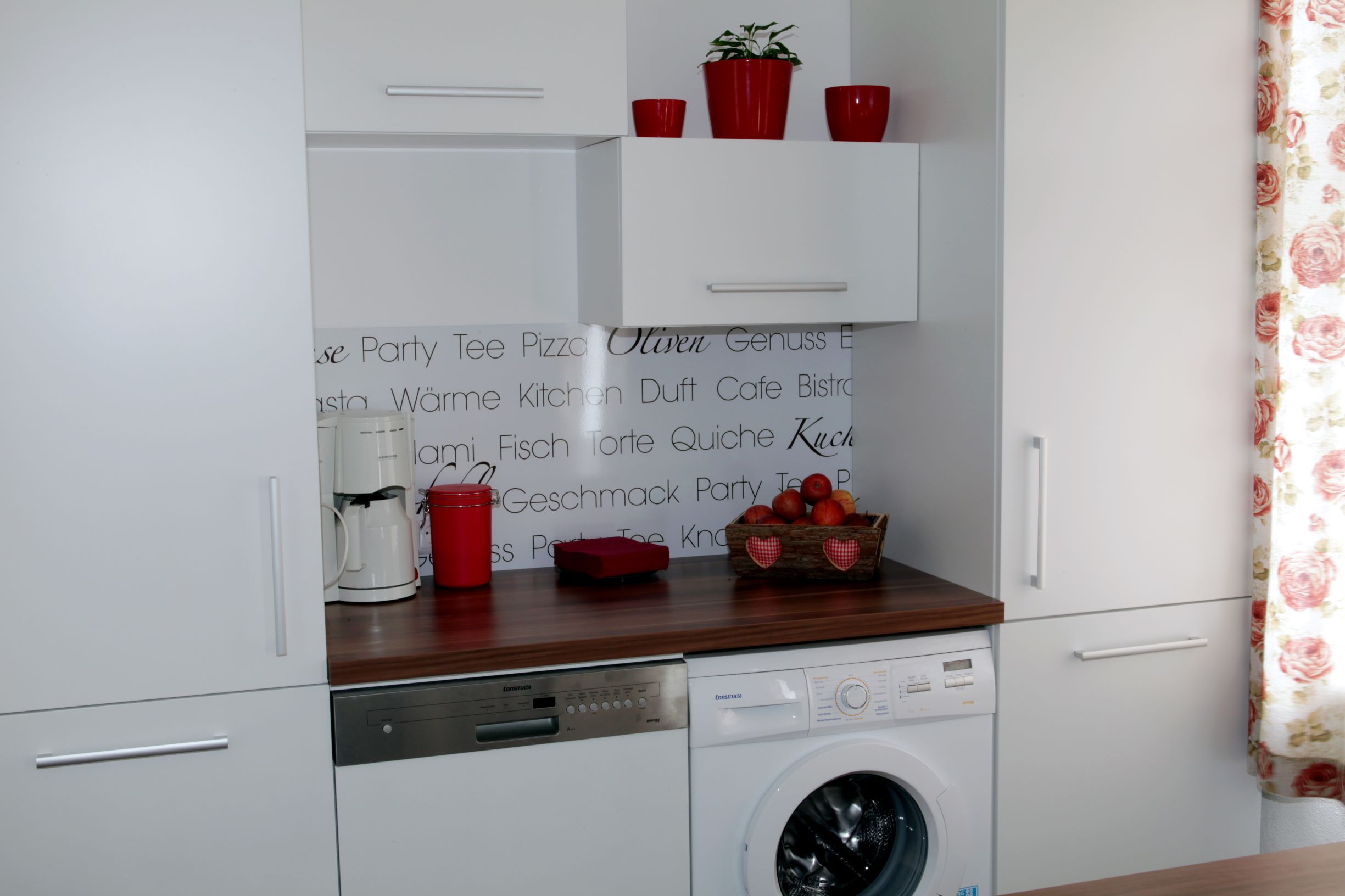 Küchenzeile mit Waschmaschine, Geschirrspüler, Kaffeemaschine und Dekoration.