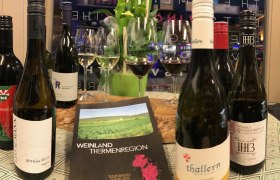 Weinflaschen und Gläser auf einem Tisch mit einem Prospekt der Weinland Thermenregion.