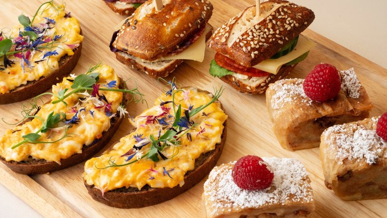 Various snacks on a wooden board, including sandwiches, sandwiches and pastries with raspberries.