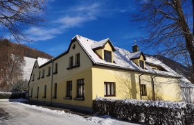 Gelbes Haus mit schneebedecktem Dach im Winter, blauer Himmel.
