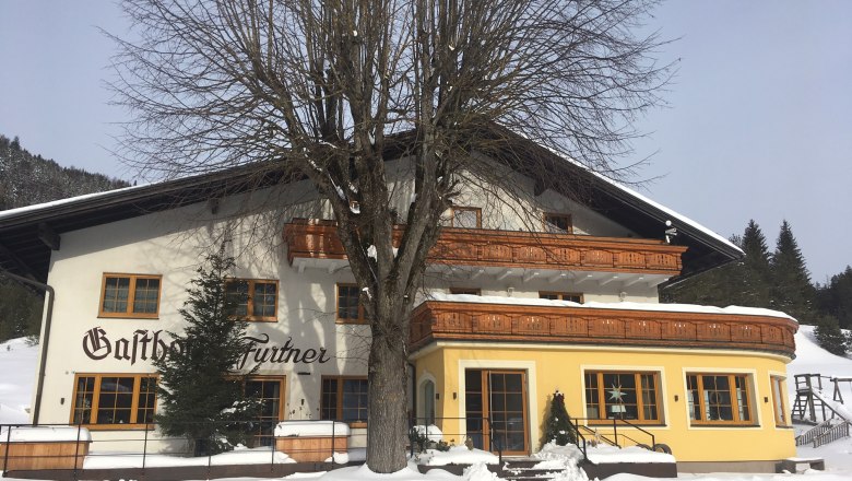 Gasthof Furtner, © Gasthof Furtner Ein Gasthof im Schnee mit Holzverzierungen und einem großen Baum davor.
