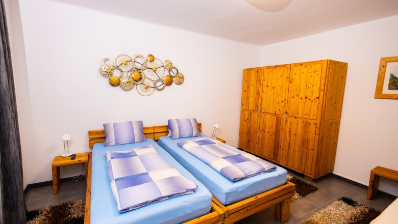 Ein gemütliches Schlafzimmer mit zwei Einzelbetten, blauer Bettwäsche, Holzmöbeln und dekorativer Wandkunst.