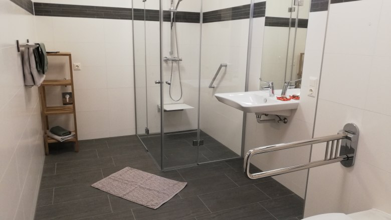 Barrier-free bathroom with shower, washbasin and grab rails.