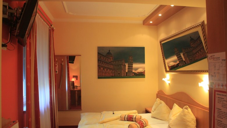 Hotel room with a double bed, pictures of the Leaning Tower of Pisa and a TV on the wall.