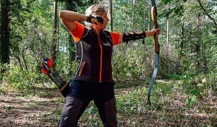 Person beim Bogenschießen im Wald mit Pfeil und Bogen.