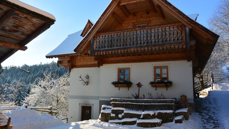 Kronaushof im Winter, © Erika Kronaus Traditionelles Haus mit Halzbalkon und weißer Fassade, umgeben von verschneiter Landschaft.
