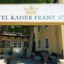 Eingang des Hotel Kaiser Franz Josef mit Schild und B&auml;umen.