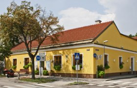 Yellow building with a red roof, signposted as Gasthaus Weidinger, on a street corner with crosswalk and traffic signs.