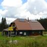 Eine Berghütte mit Solarpanelen auf dem Dach, umgeben von Wiesen und Wald.