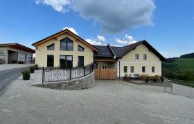 Yellow house with large windows on a paved area under a blue sky.