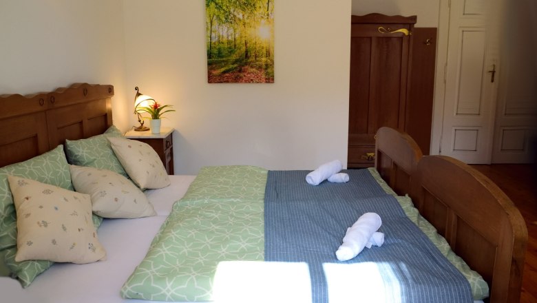 Gemütliches Doppelzimmer mit Holzmöbeln, grünem Bettzeug und einem Bild an der Wand.