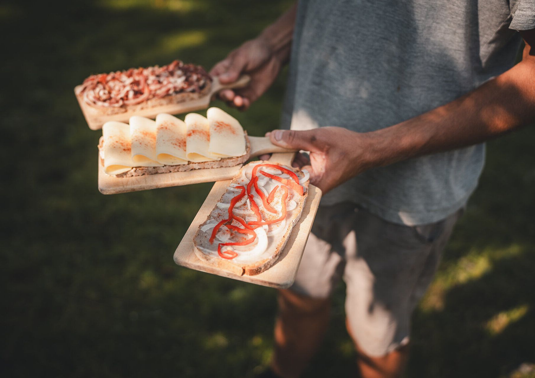 Person trägt ein Holzbrett mit traditioneller Hüttenjause auf der Herrenalm. 