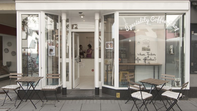 Exterior view of a caf&eacute; with tables and chairs on the sidewalk.