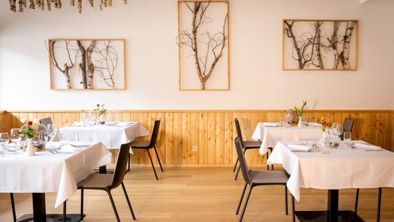 Elegantes Restaurant mit Holzwänden, weißen Tischdecken und Birkenkunst an den Wänden.