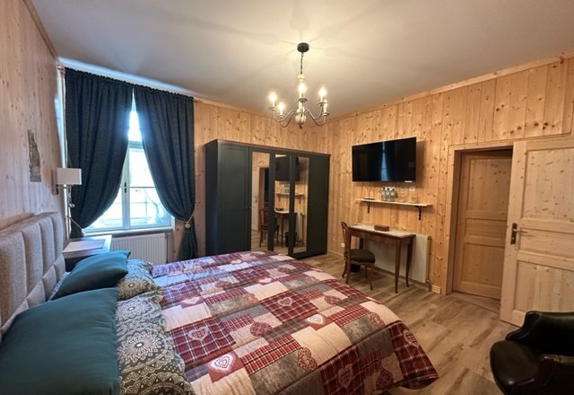 Gemütliches Hotelzimmer mit Holzwänden, Doppelbett, Schreibtisch, Kleiderschrank und Flachbildfernseher.