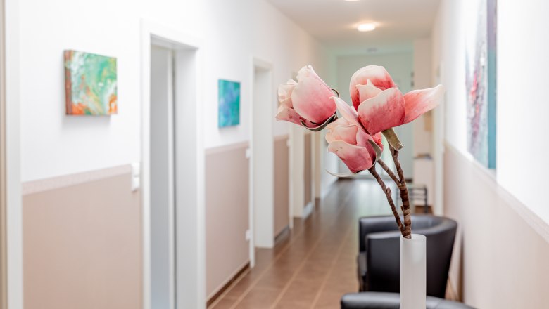 Ein heller Flur mit weißen Wänden, dekoriert mit Kunstwerken und einer Vase mit rosa Blumen im Vordergrund.
