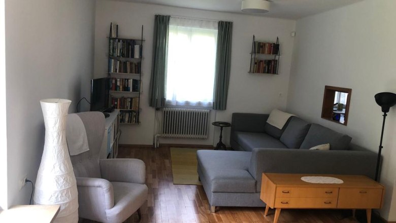 Ein Wohnzimmer mit grauem Sofa, Sessel, Bücherregalen und Holzboden.