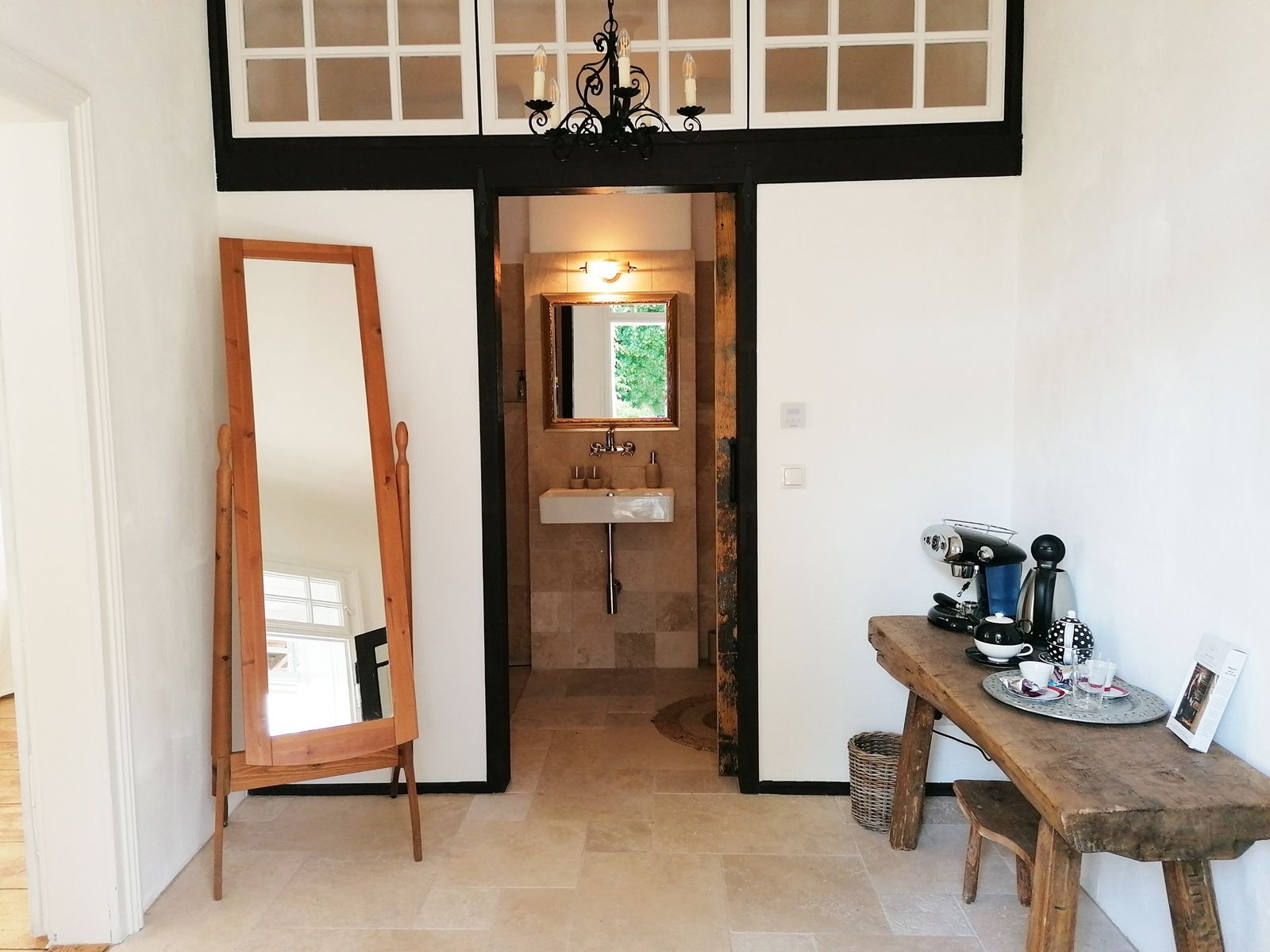 Ein Vorraum mit einem großen Spiegel, einer Kaffeemaschine auf einem Holztisch und einem Waschbecken im Hintergrund.