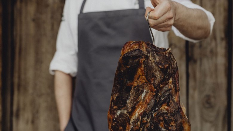 Person h&auml;lt ger&auml;ucherten Schinken an einem Haken.