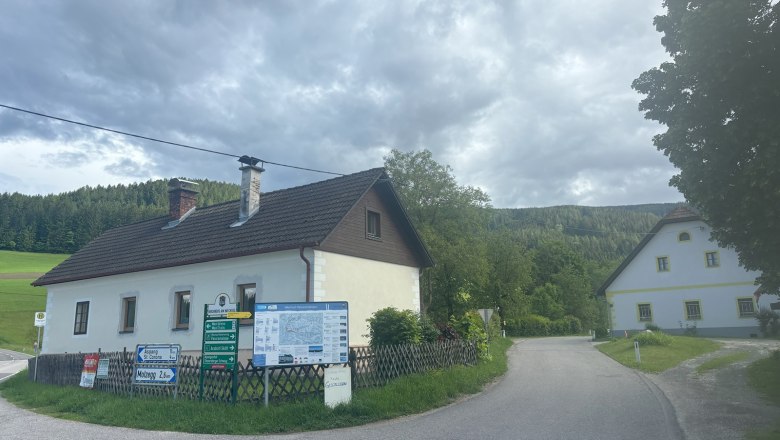 Ferienhaus Hofer, © Michael Hofer Ländliche Straße mit zwei Häusern und Wegweisern, umgeben von Wäldern und Wiesen.