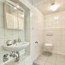 Modern bathroom with white tiles, washbasin, mirror and toilet.