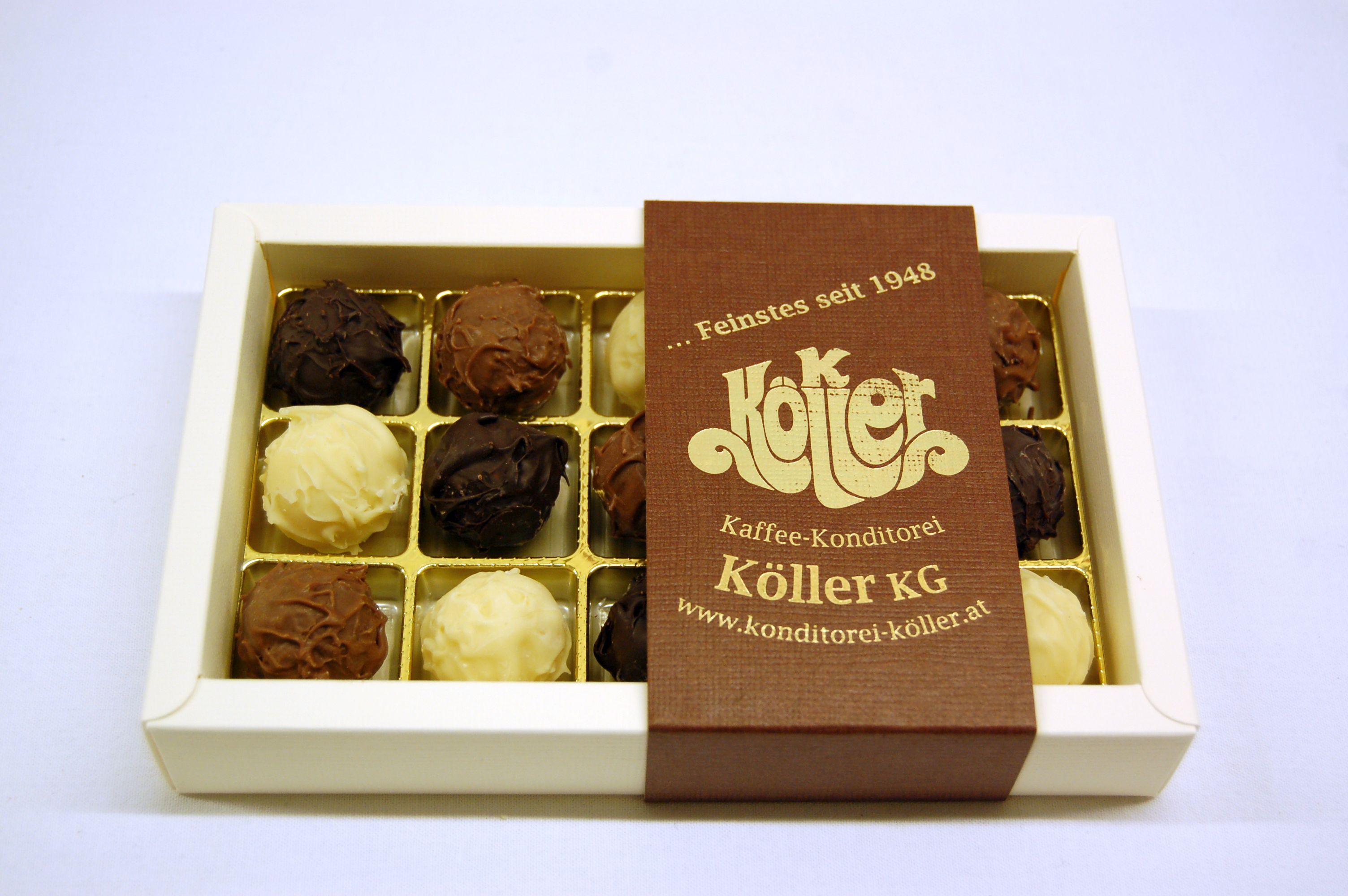 Eine Schachtel mit handgemachten Pralinen von Köller KG, teilweise geöffnet, auf weißem Hintergrund.