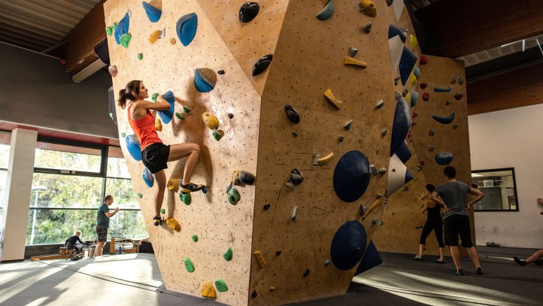 Person klettert an einer Indoor-Kletterwand mit bunten Griffen.