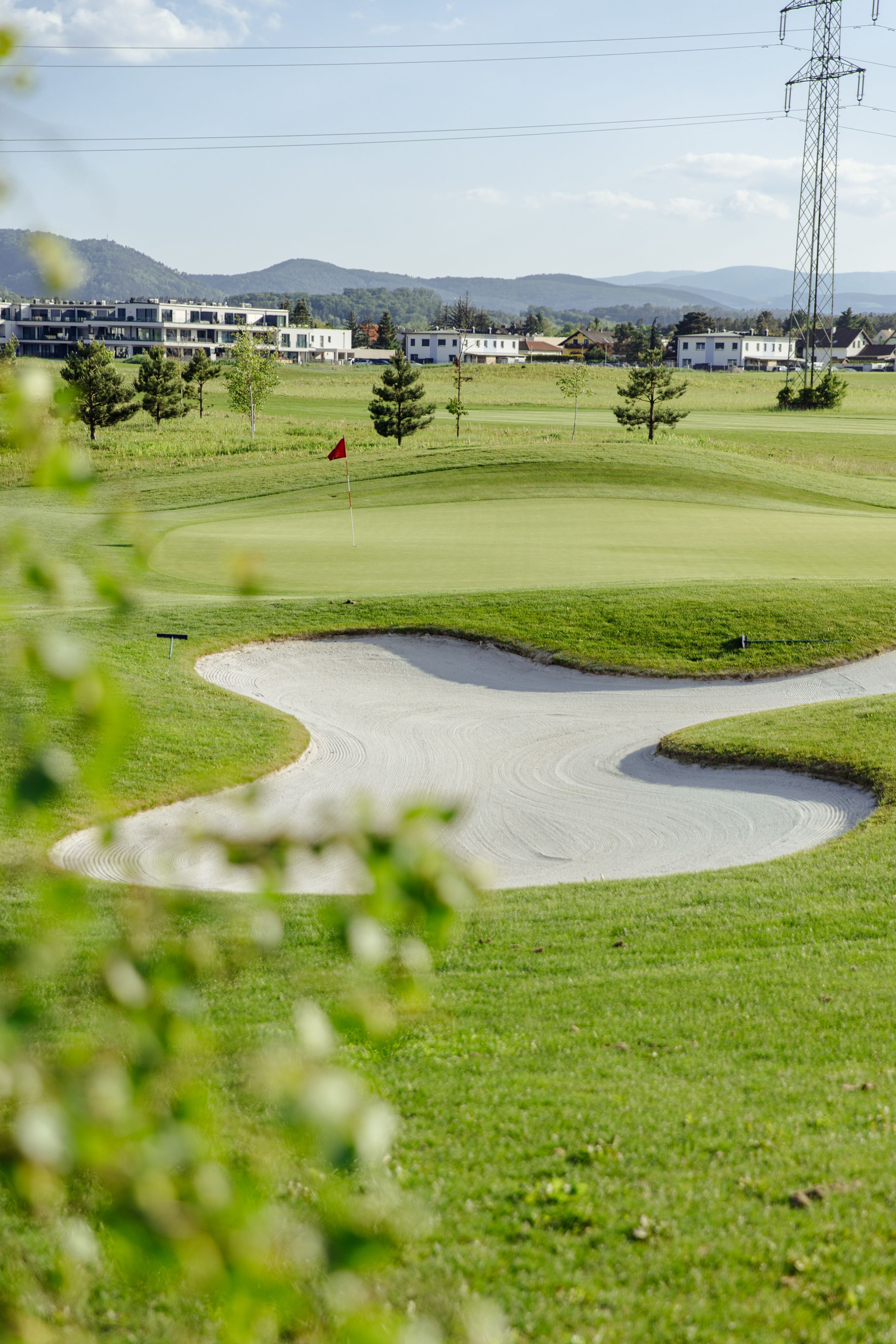 Blick auf ein Golffeld mit Sandbecken und roter Fahne, die ein Loch markiert.