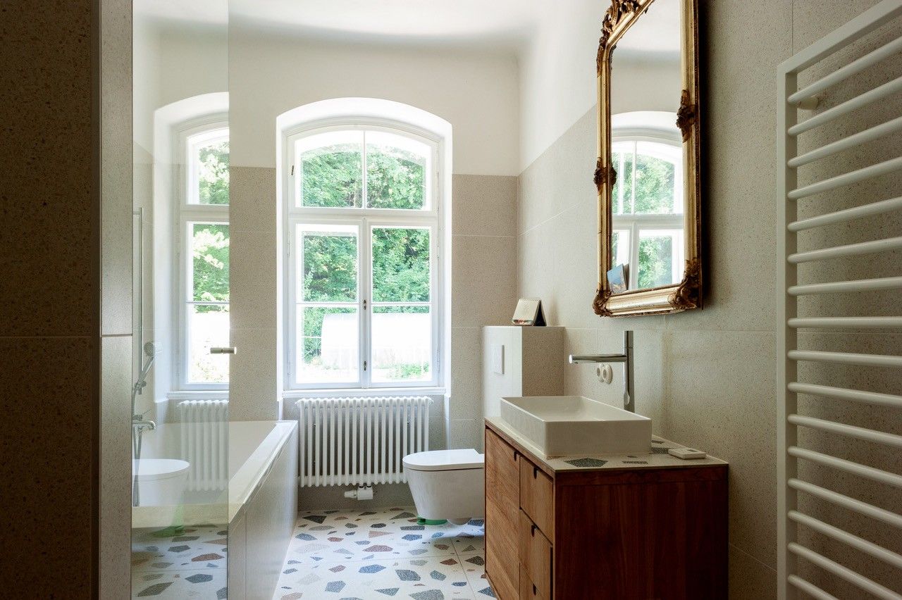 Ein elegantes Badezimmer mit Badewanne, Waschbecken, großem Spiegel und zwei Fenstern mit Blick ins Grüne.