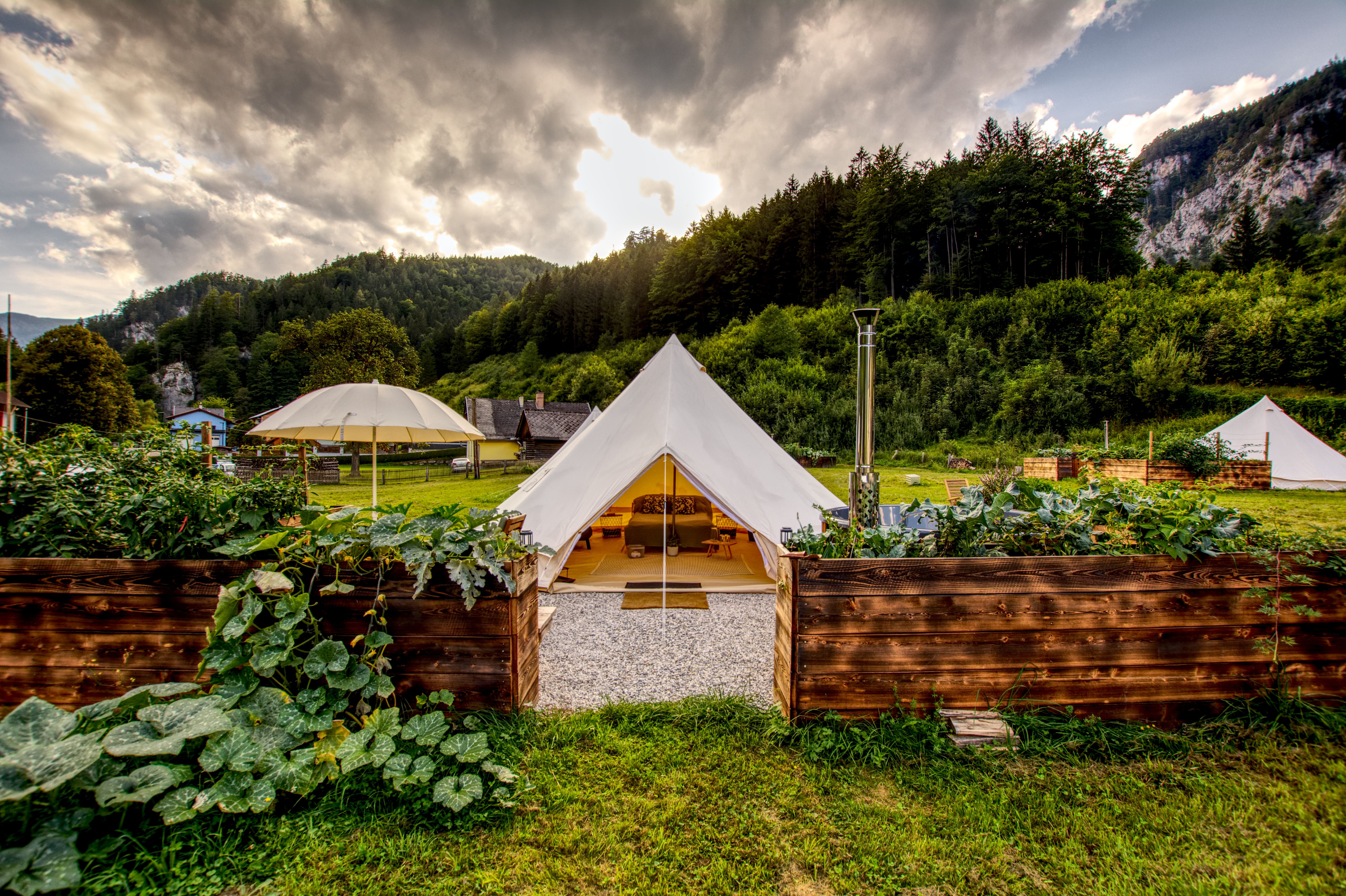 Glamping-Zelt in grüner Landschaft mit Bergen im Hintergrund.