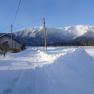 Snowy landscape with a house and mountains in the background.