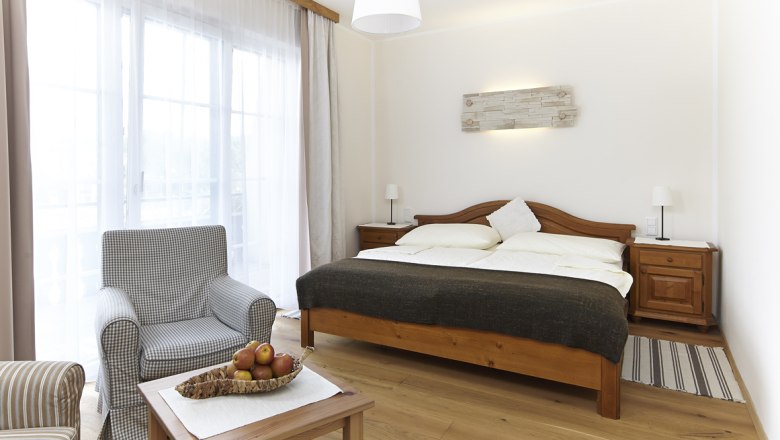 Bright room with double bed, armchair and table with fruit bowl.