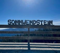 Ausblick auf Sonnenschein und blauenhimmel von der Pollereshütte, davor ein Zaun mit dem Schriftzug "SONNWENDSTEIN"