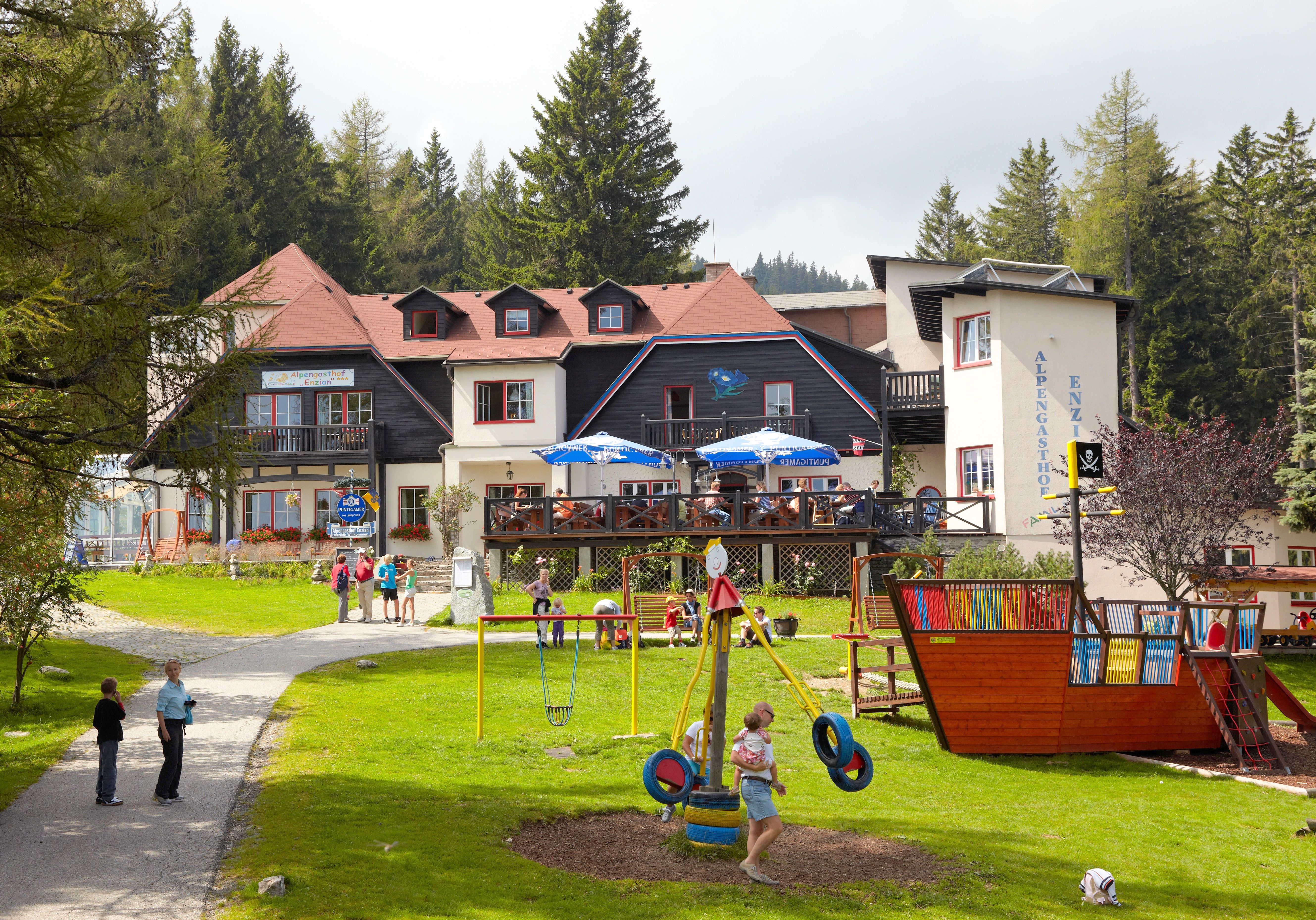 Ein Gasthof in den Alpen mit Spielplatz und Menschen im Freien.