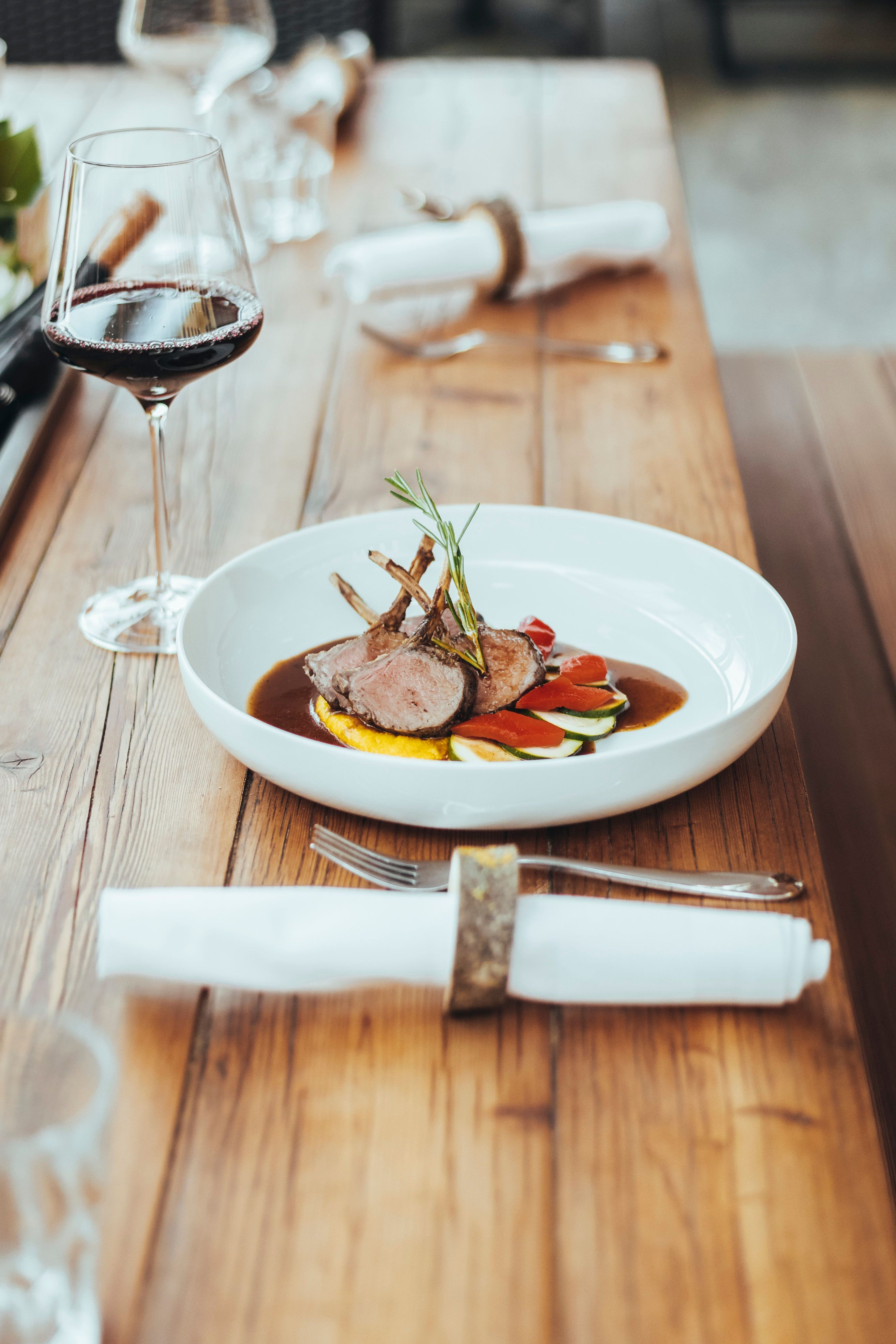 Ein Holztisch mit einem Teller mit einem Gourmetgericht, einem Weinglas, Besteck und Servietten.