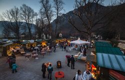 Adventmarkt im Schloss Reichenau an der Rax. Das Schloss ist von außen stimmungsvoll beleuchtet, im Innenhof stehen die Hütten. Menschen stehen davor und trinken Punsch.