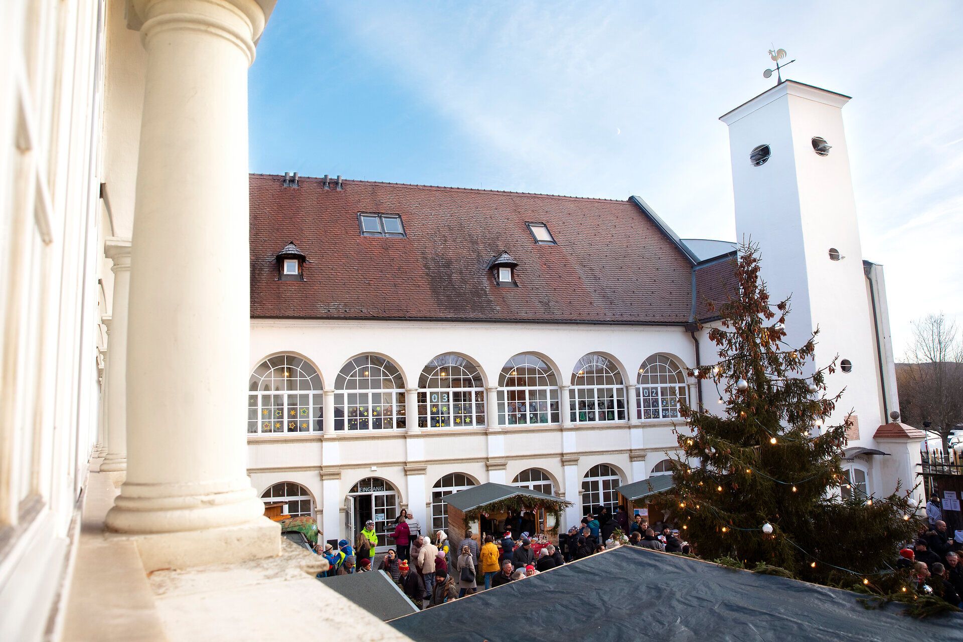 Innenhof eines historischen Gebäudes mit Weihnachtsbaum und Marktständen bei Tageslicht.