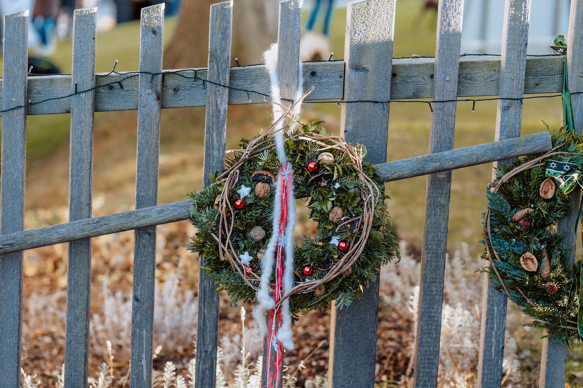 Weihnachtlicher Türkranz mit roten Bändern an einem rustikalen Holzzaun.