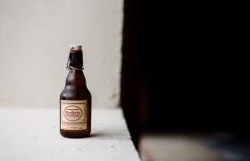 A bottle of RaxBr&auml;u Helles Bier on a white surface against a dark background.