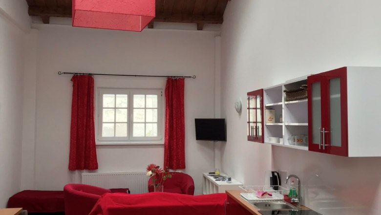 Wohn- und Essbereich in einem Loft mit roten Möbeln und Holzbalkendecke.