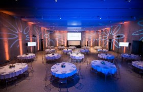 Ein eleganter Veranstaltungsraum mit runden, gedeckten Tischen und blauer Beleuchtung.