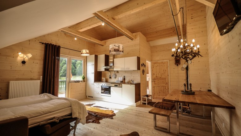 Gemütliches Apartment mit Holzwänden, Küche, Esstisch und Bett.