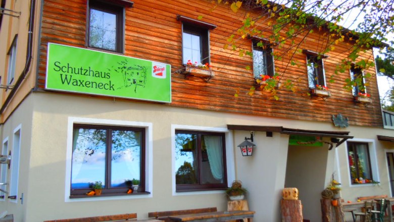 Eingang zum Schutzhaus Waxeneck, © Waxeneckhaus Eingang zum Schutzhaus Waxeneck mit Holztischen und Blumenkästen.